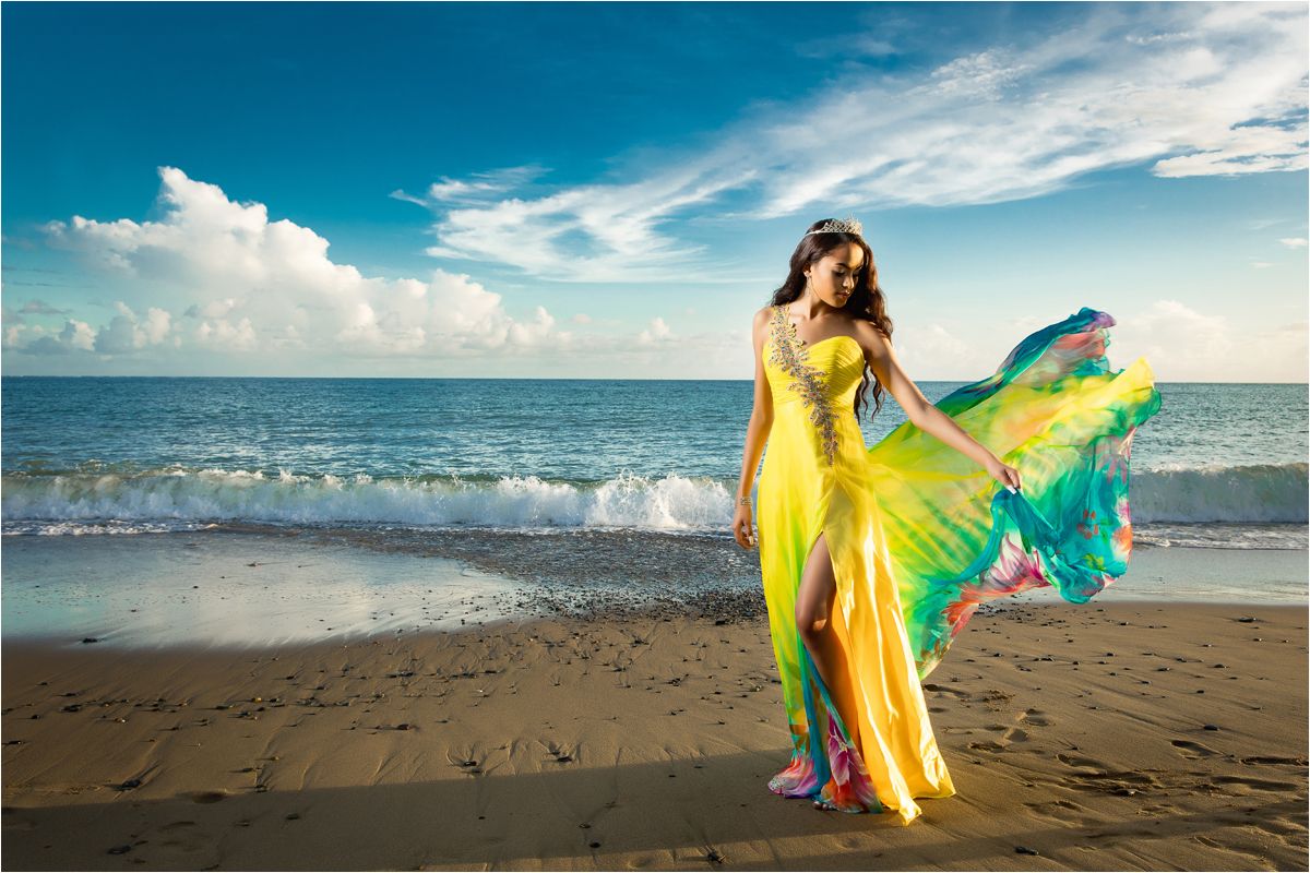 A person in a flowing yellow dress dances gracefully along a sandy beach at sunset with ocean waves in the background.