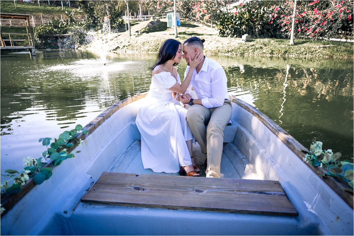 A romantic boat scene with a couple in wedding attire sitting together in a decorated rowboat on a serene pond.