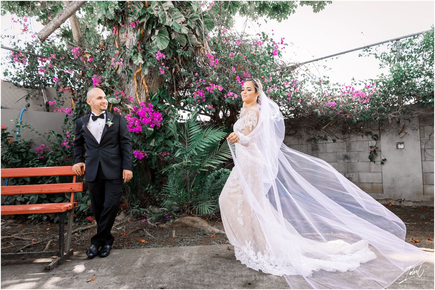 A wedding couple poses separately with the bride's dramatic veil flowing in a garden setting.