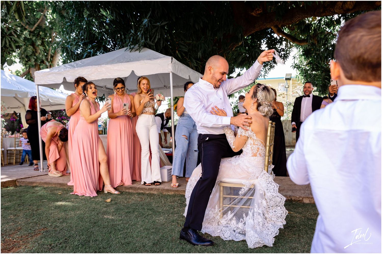 Wedding reception outdoors with guests in pink dresses watching celebration on lawn.