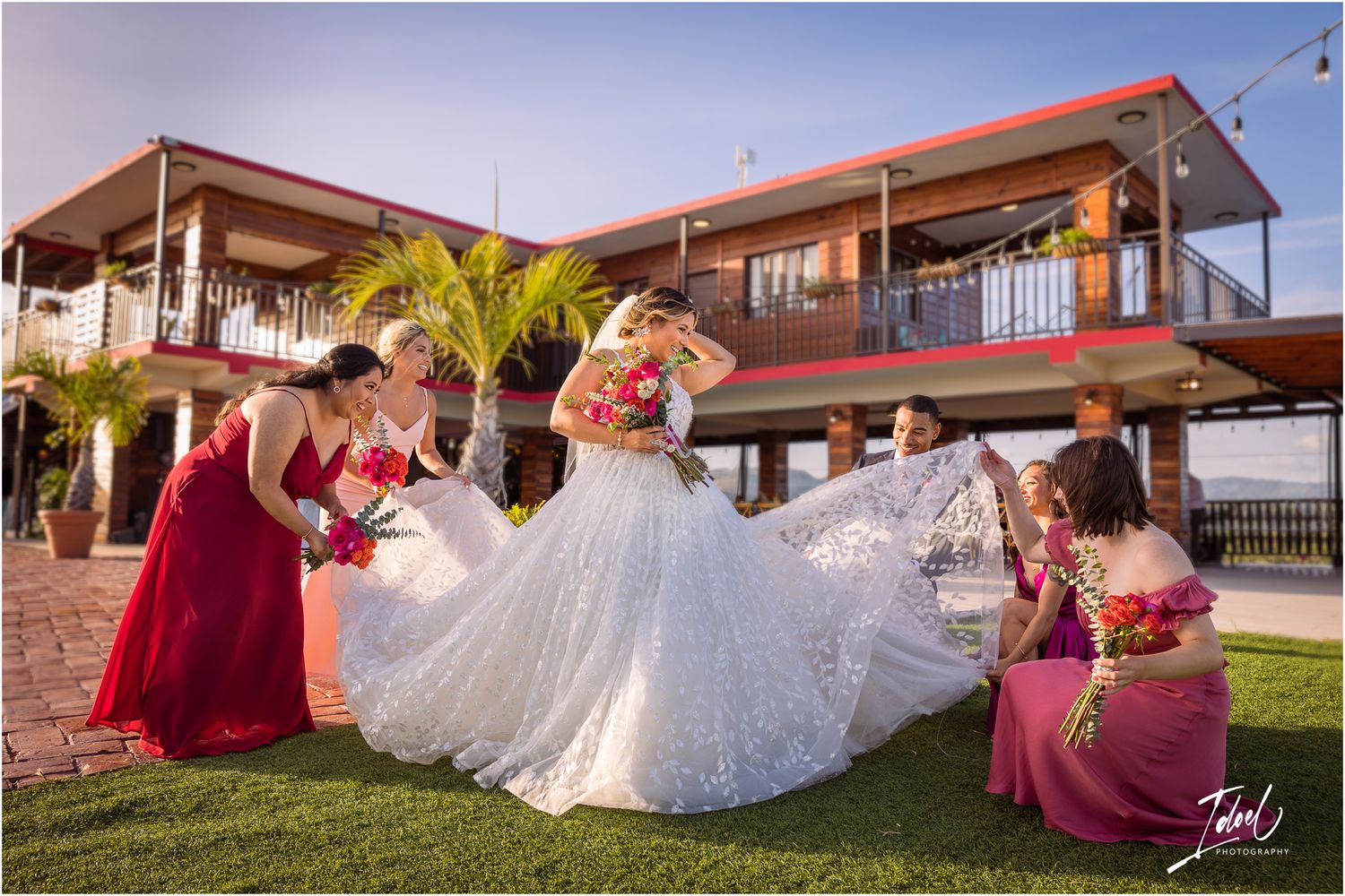 Wedding party fluffs white ballgown dress on green lawn with two-story venue in background.