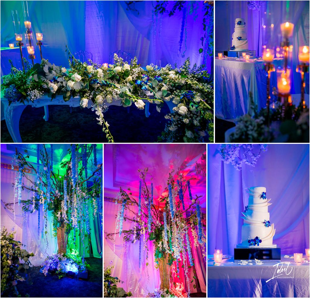 Wedding reception decor features cascading floral arrangements illuminated by dramatic blue and purple uplighting and chandeliers.