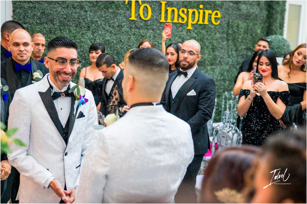 Two people wearing formal attire share an emotional moment during a wedding ceremony as guests look on and applaud.
