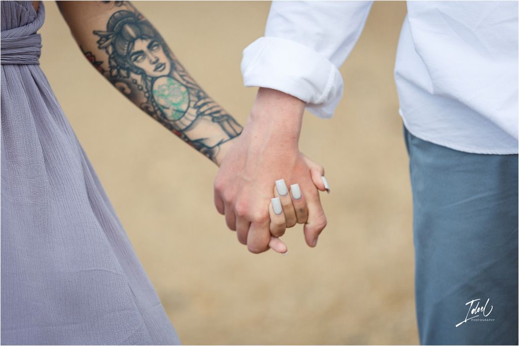 Close-up of couple holding hands with visible tattoo artwork and rings.