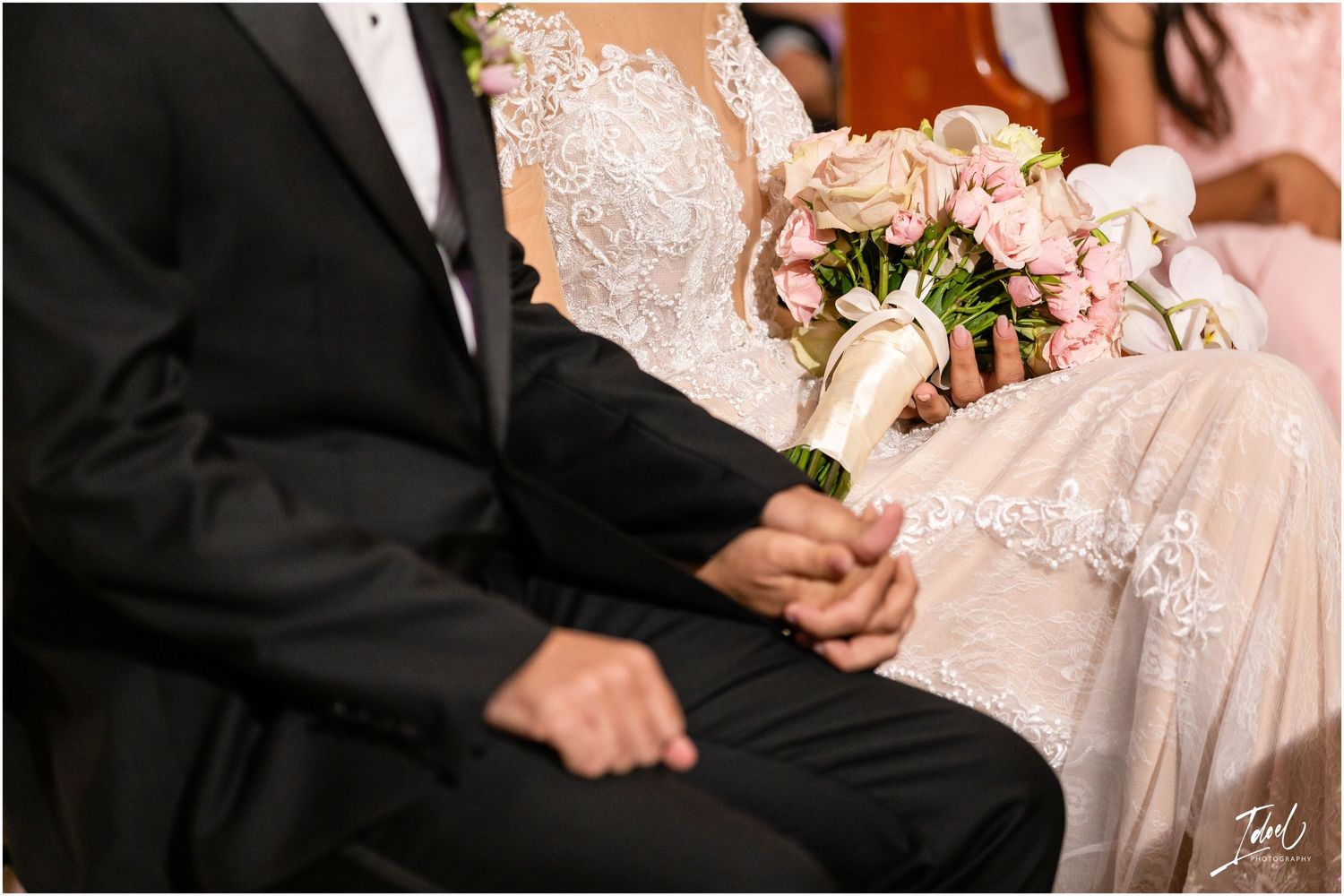 Close-up detail of wedding couple showing lace dress and black tuxedo during ceremony.