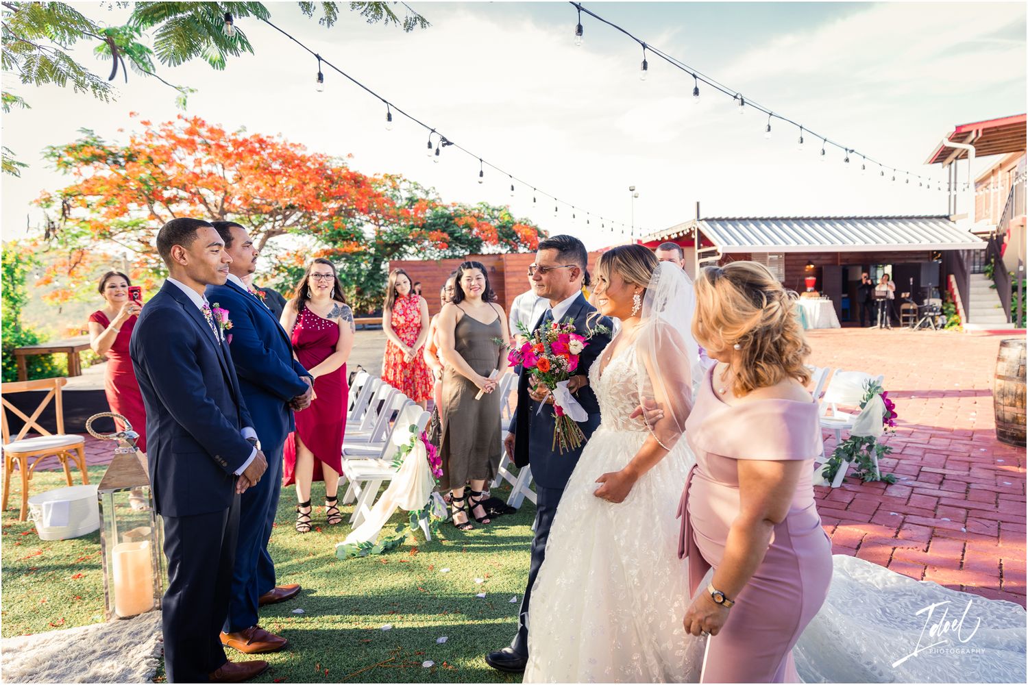 Outdoor wedding gathering with string lights and a red flowering tree creating a festive atmosphere.