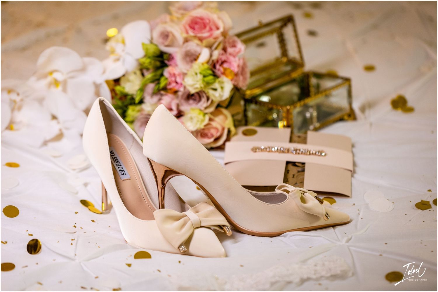 Elegant cream bridal shoes with bows displayed next to pink roses and scattered gold confetti.