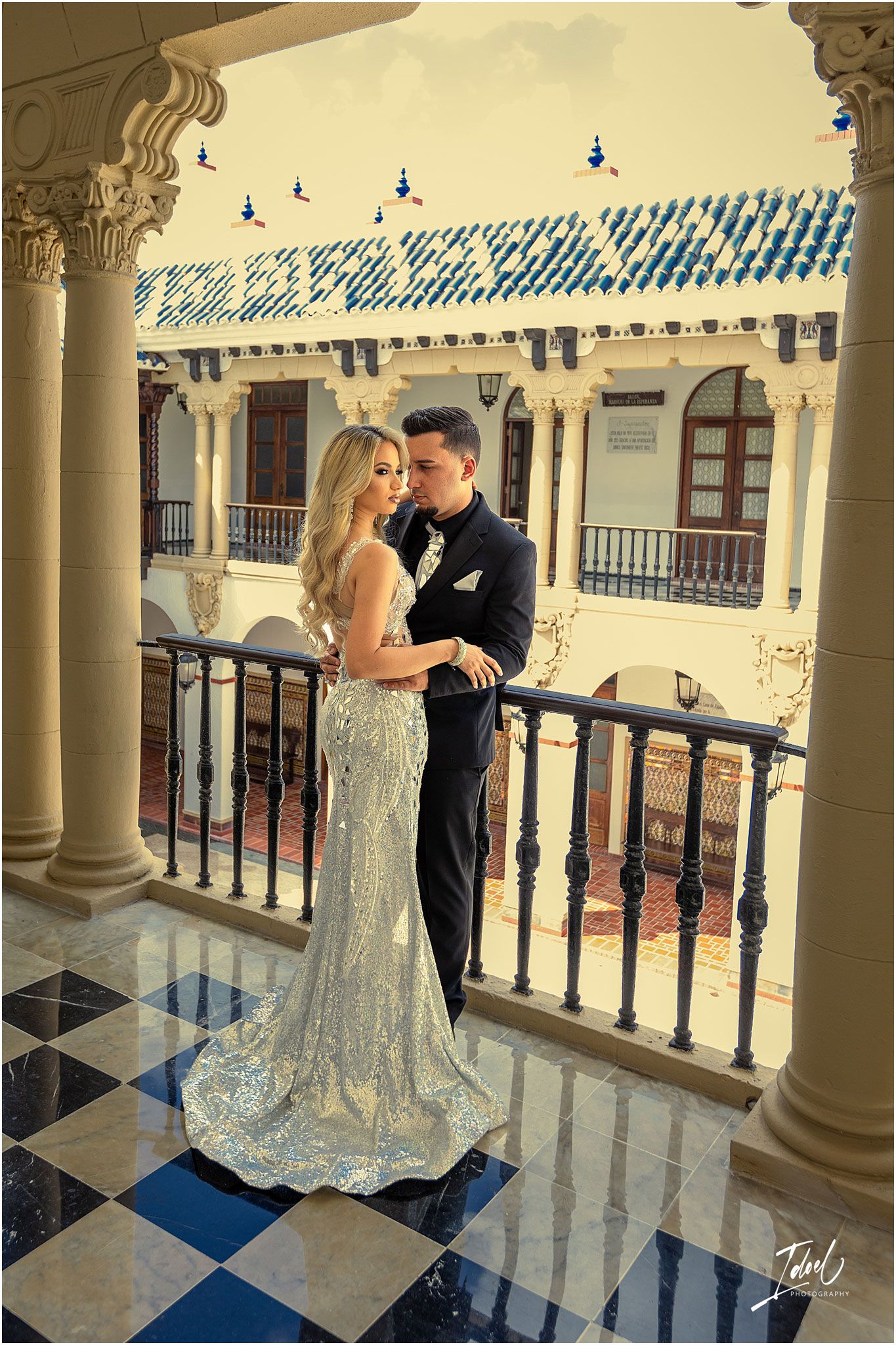 Glamorous couple poses on balcony with decorative Spanish colonial architecture.