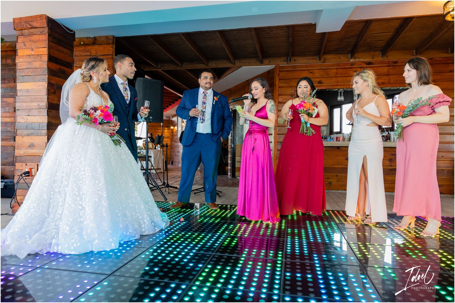 Wedding party gathered on an illuminated LED dance floor with vibrant pink and red attire.