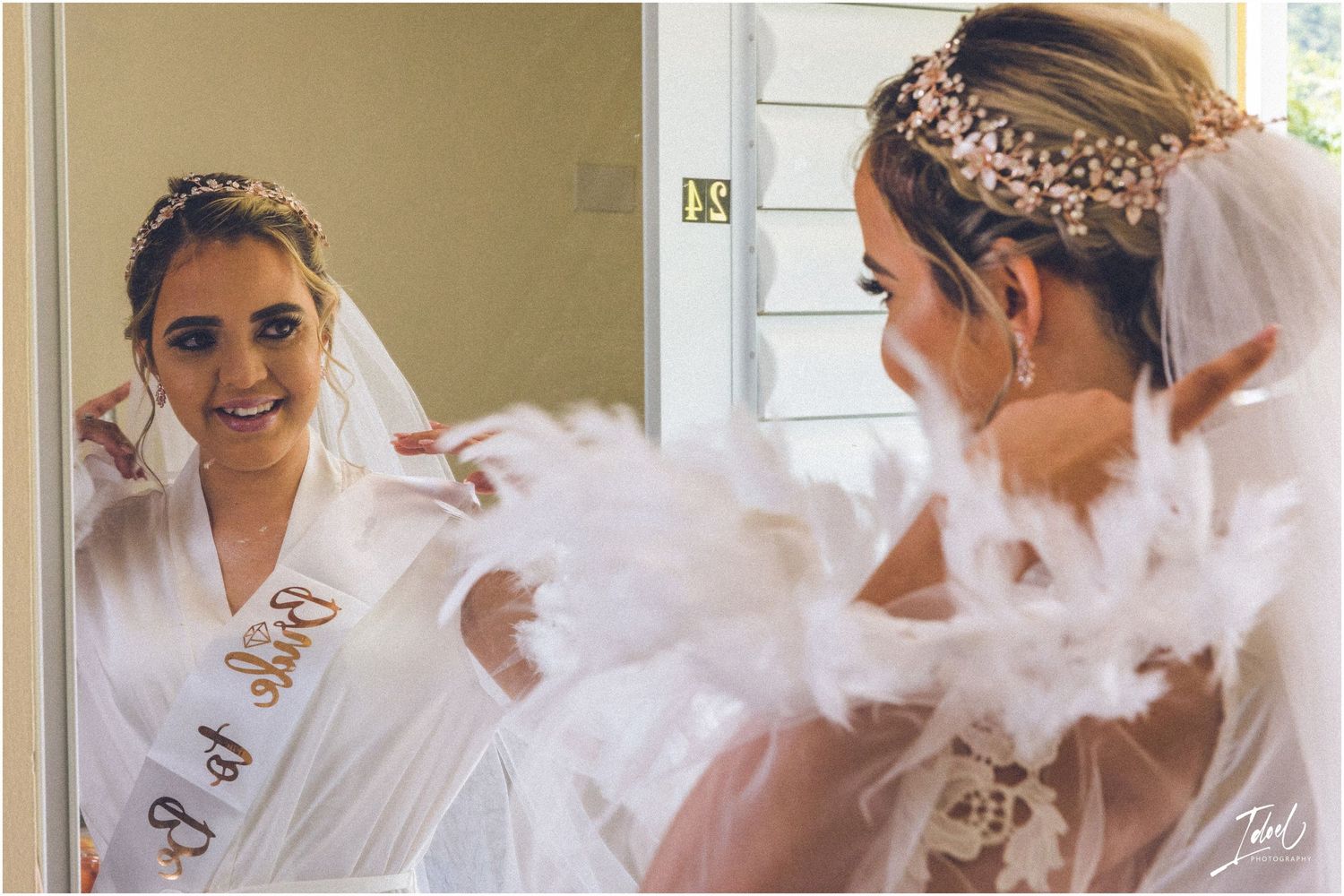 Bride in white robe looking at her reflection in mirror during wedding preparations.