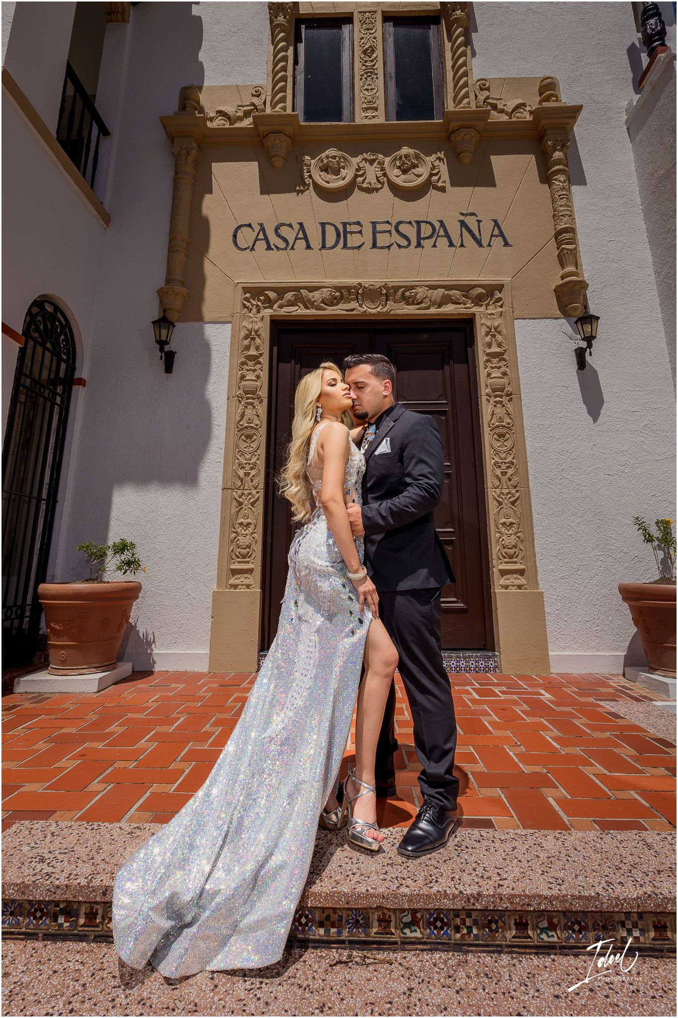 Glamorous couple in formal wear posing at the Casa de España entrance with Spanish colonial architecture.