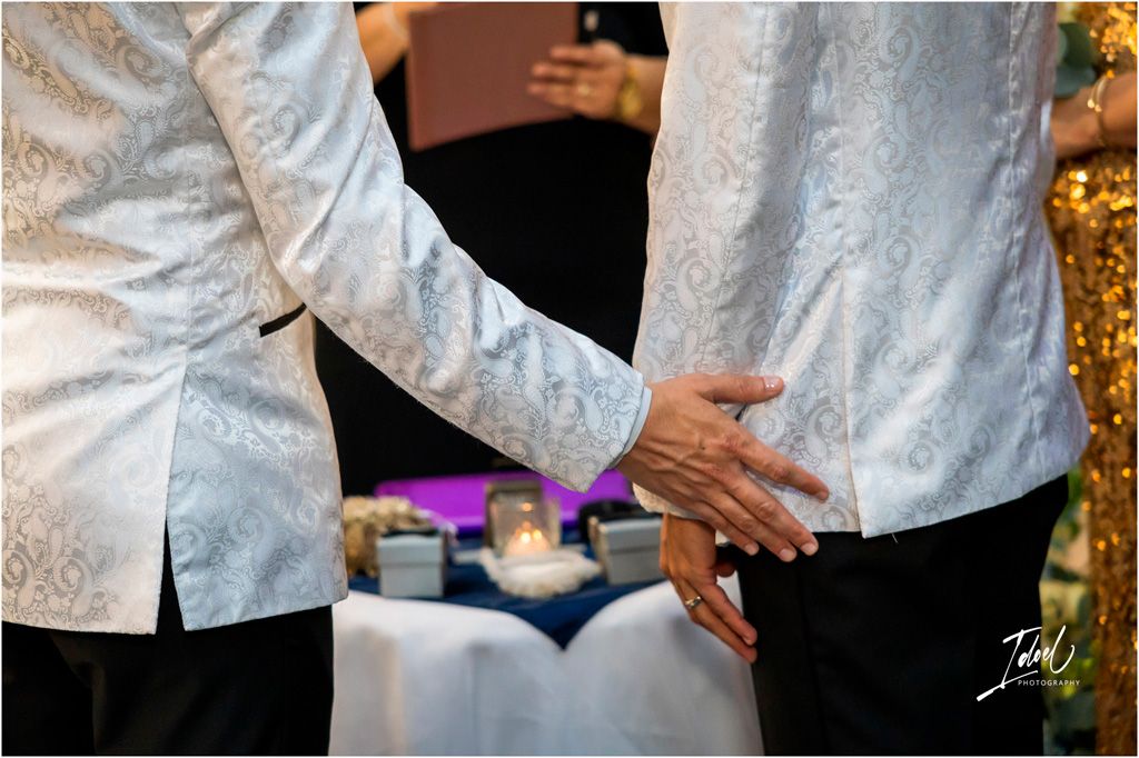 Close-up shot of hands wearing white lace outfits at a formal party with blurred sparkly background.