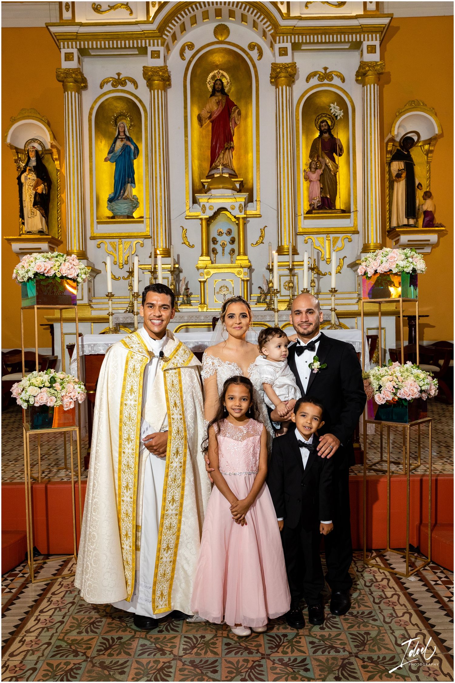 Formal group portrait in front of ornate church altar with religious artwork.