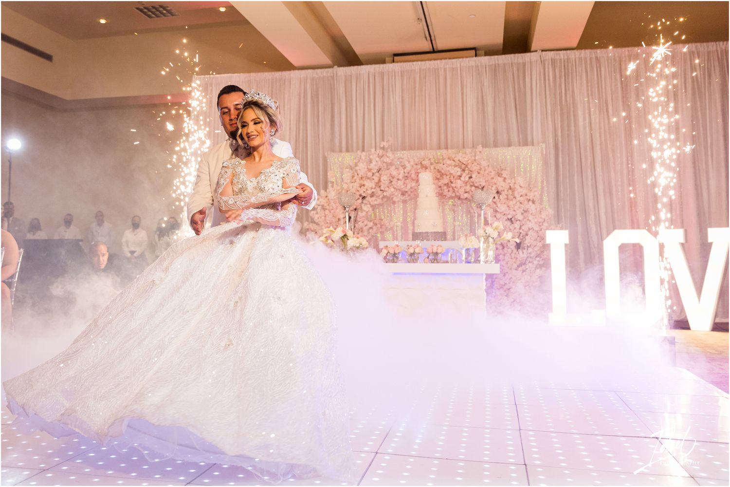 A romantic wedding dance moment on an illuminated dance floor with fog and LOVE sign backdrop.