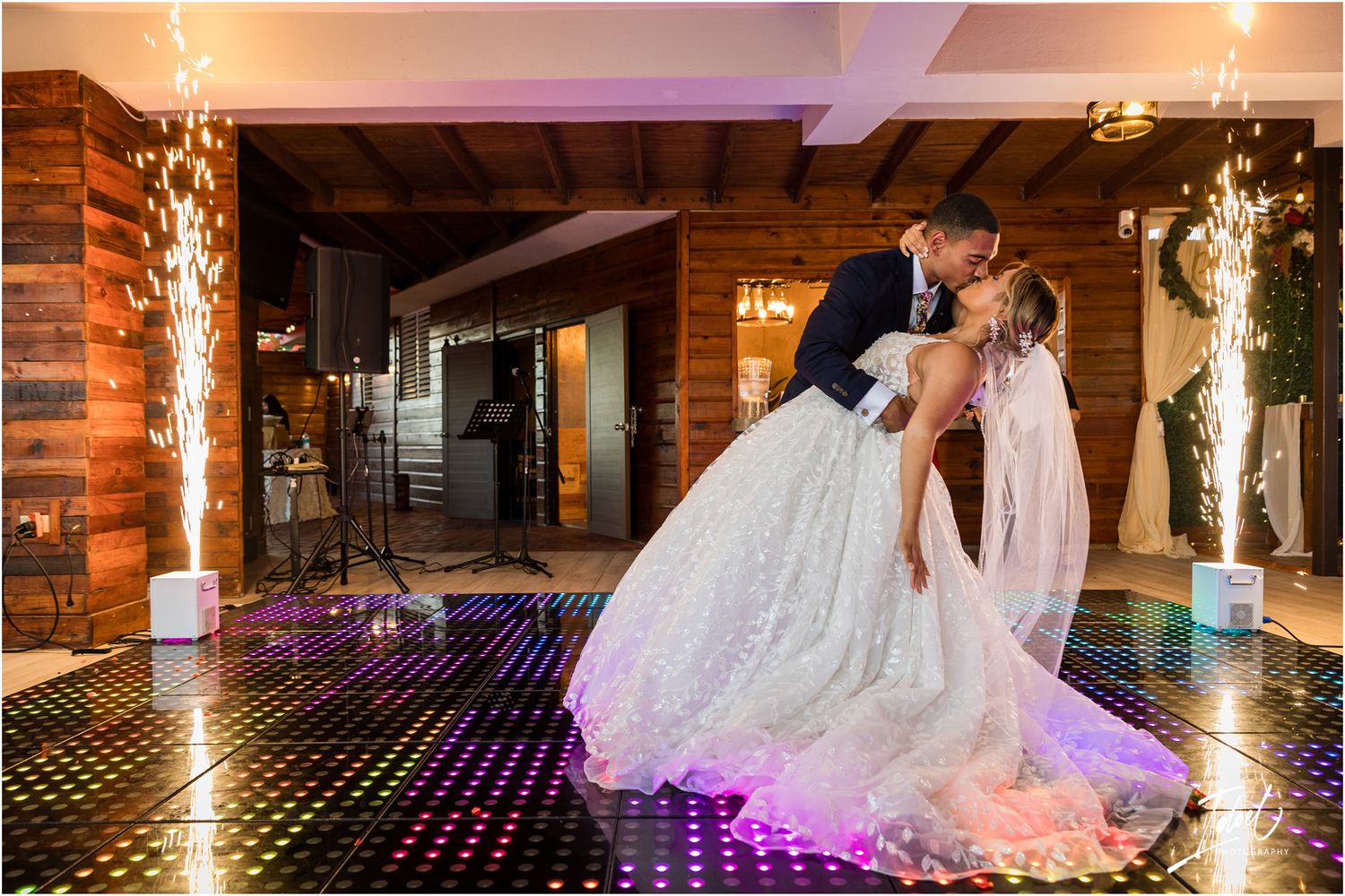Dramatic dip dance move on illuminated LED floor with sparkler pillars in rustic venue.