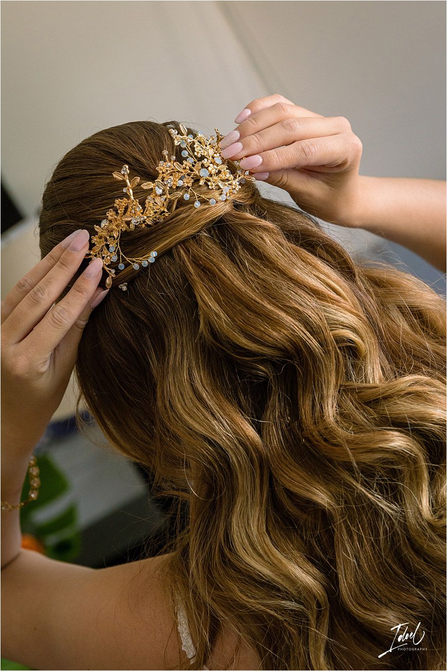 Close-up of hands placing an ornate gold floral hairpiece on wavy blonde hair.