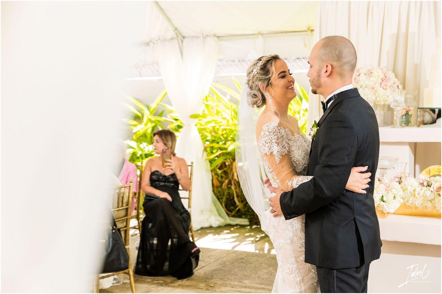 Romantic dancing moment captured at outdoor wedding reception with tropical greenery backdrop.