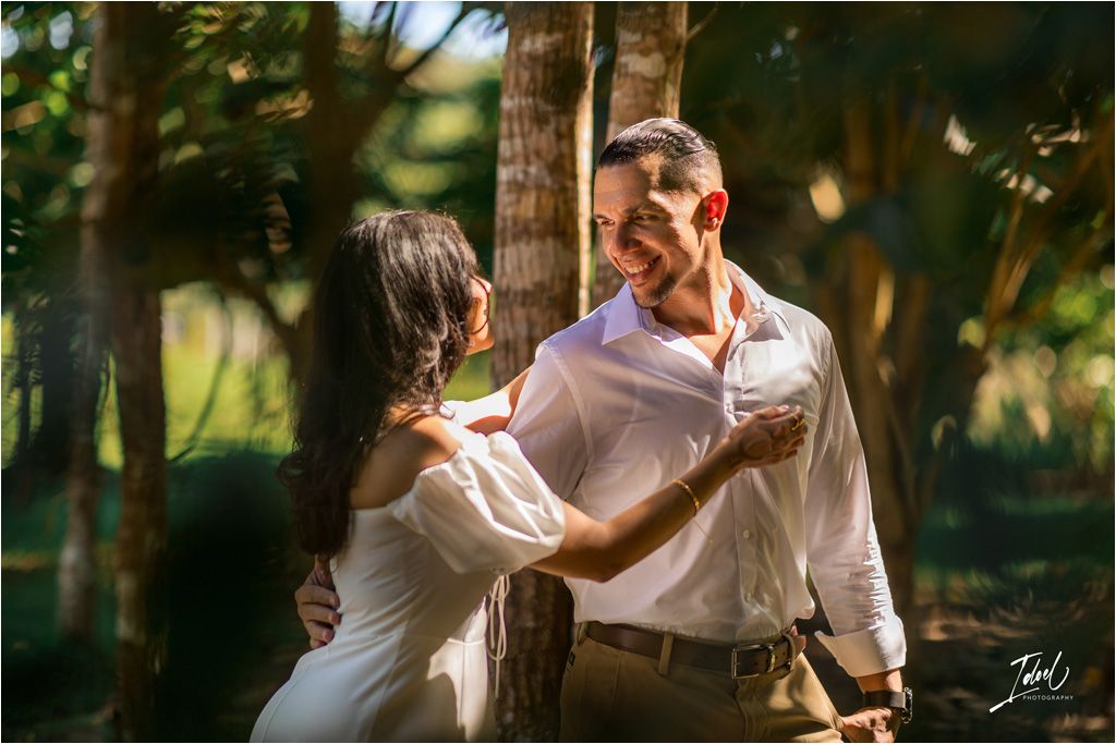 A romantic couple shares an intimate moment while dancing together in a sunlit wooded setting.