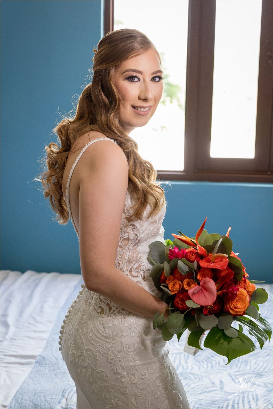 Bride poses with colorful bouquet in front of window in blue room.