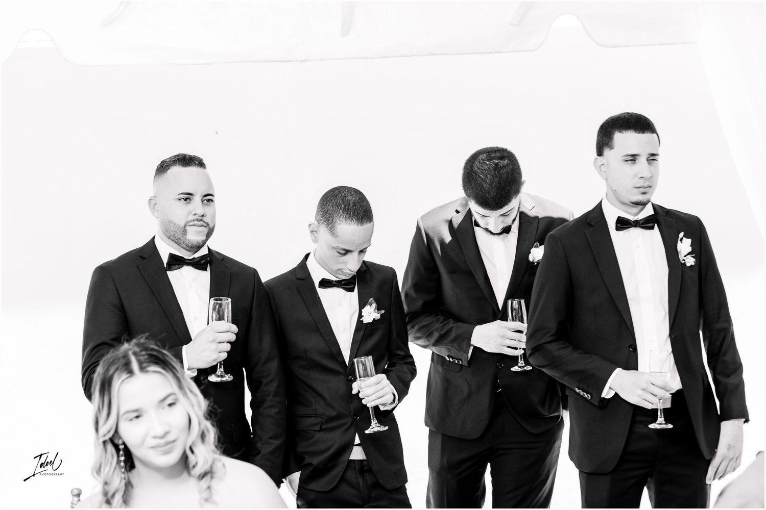Black and white photo of groomsmen in tuxedos holding champagne glasses at wedding celebration.