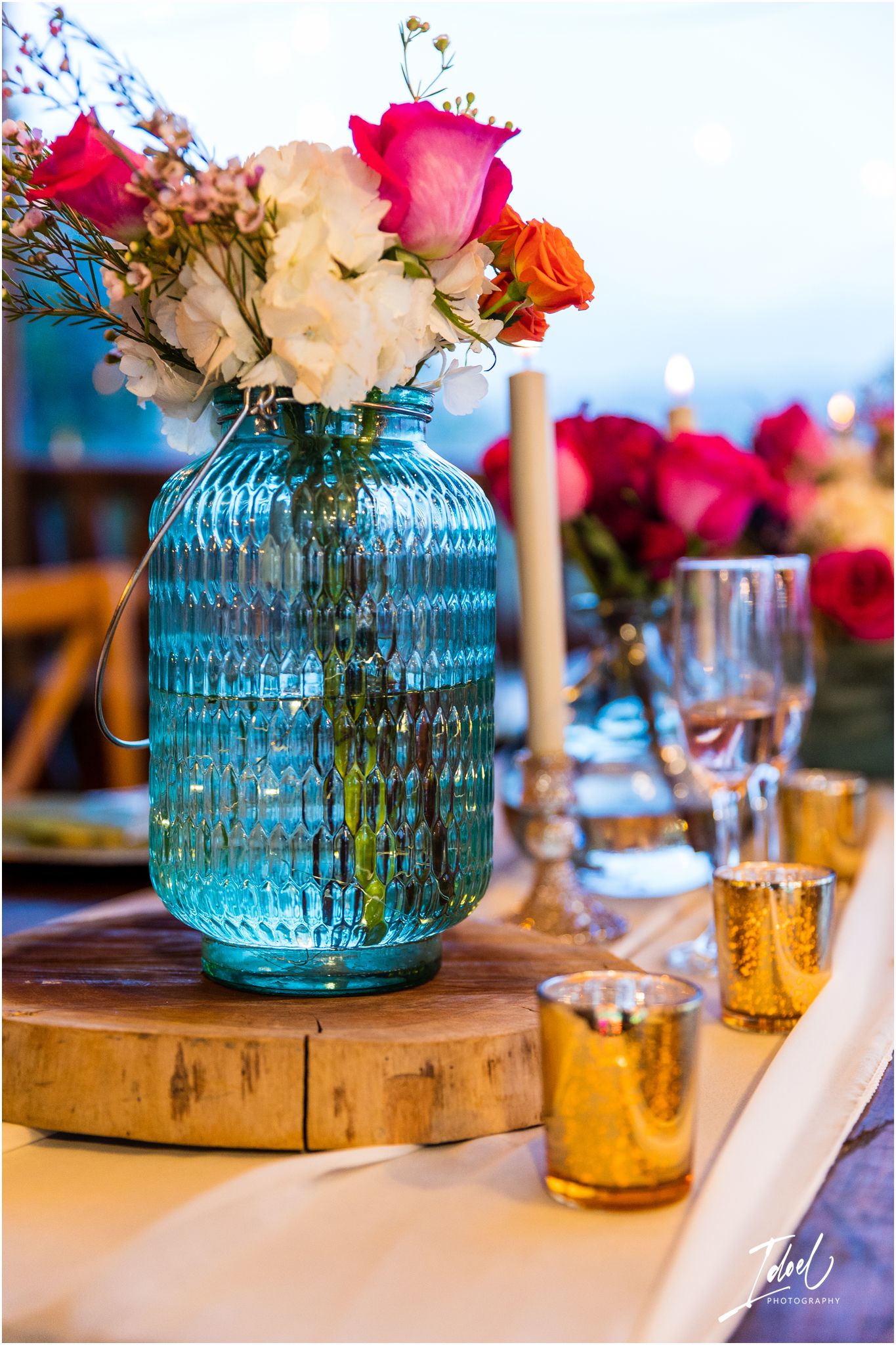 Colorful roses in a blue glass vase with gold accents on a wooden table setting.