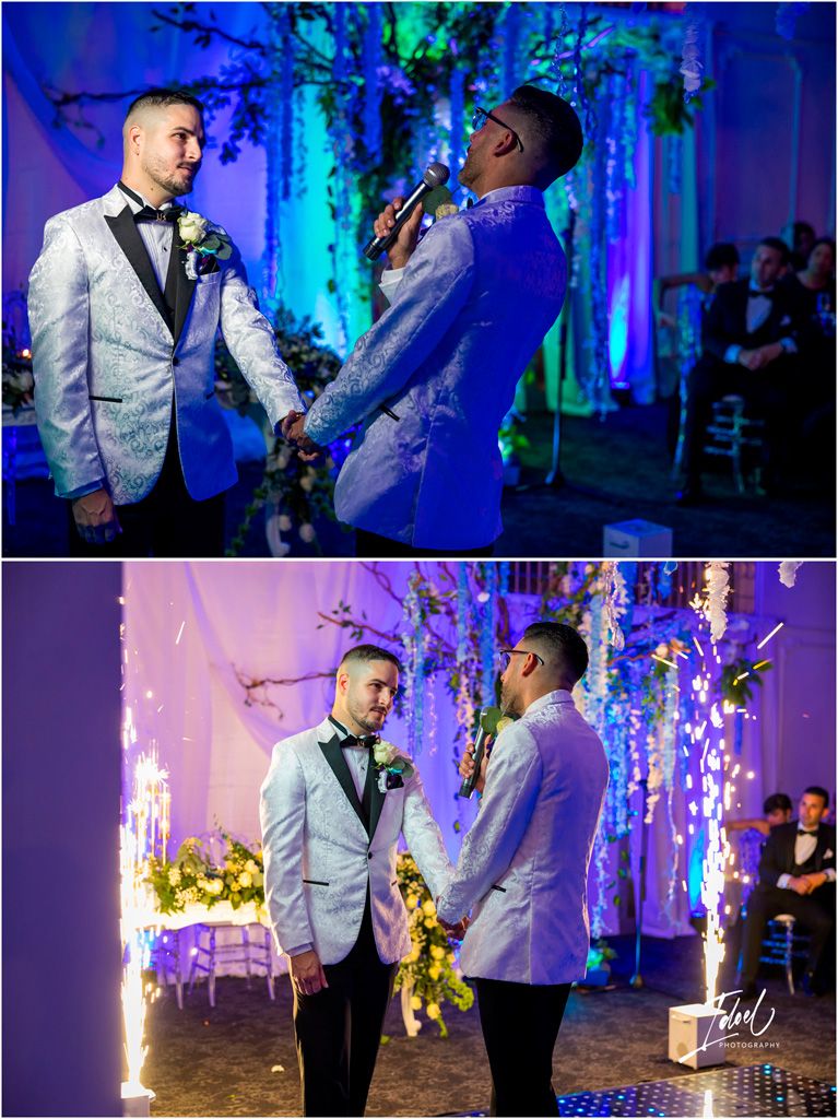 Two people in light suits hold hands and exchange vows during a wedding ceremony with blue and purple lighting decor.