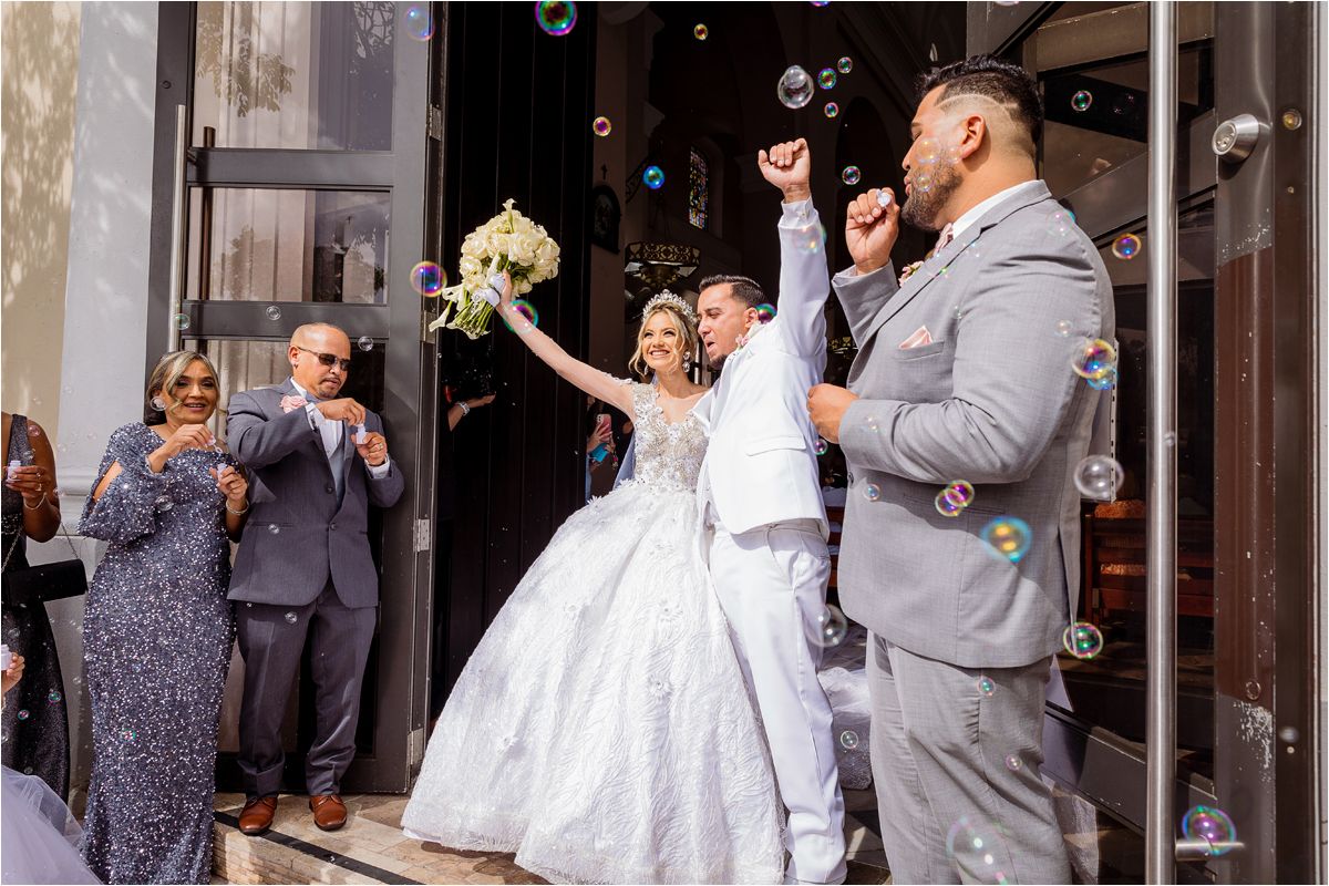Wedding guests blow bubbles as newlyweds exit their ceremony in a joyful celebration.