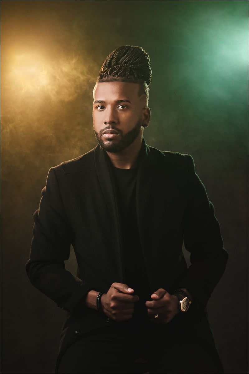 Professional portrait against dramatic gold and teal lighting with figure wearing black blazer and stylish braided hairstyle.