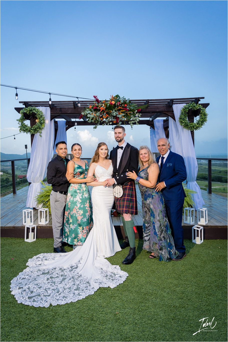 Wedding party gathered on a scenic outdoor deck with mountain views and floral decorations.