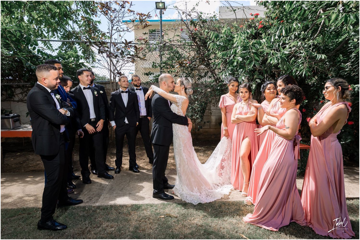Wedding ceremony moment with bridal party in pink dresses and groomsmen in black tuxedos.