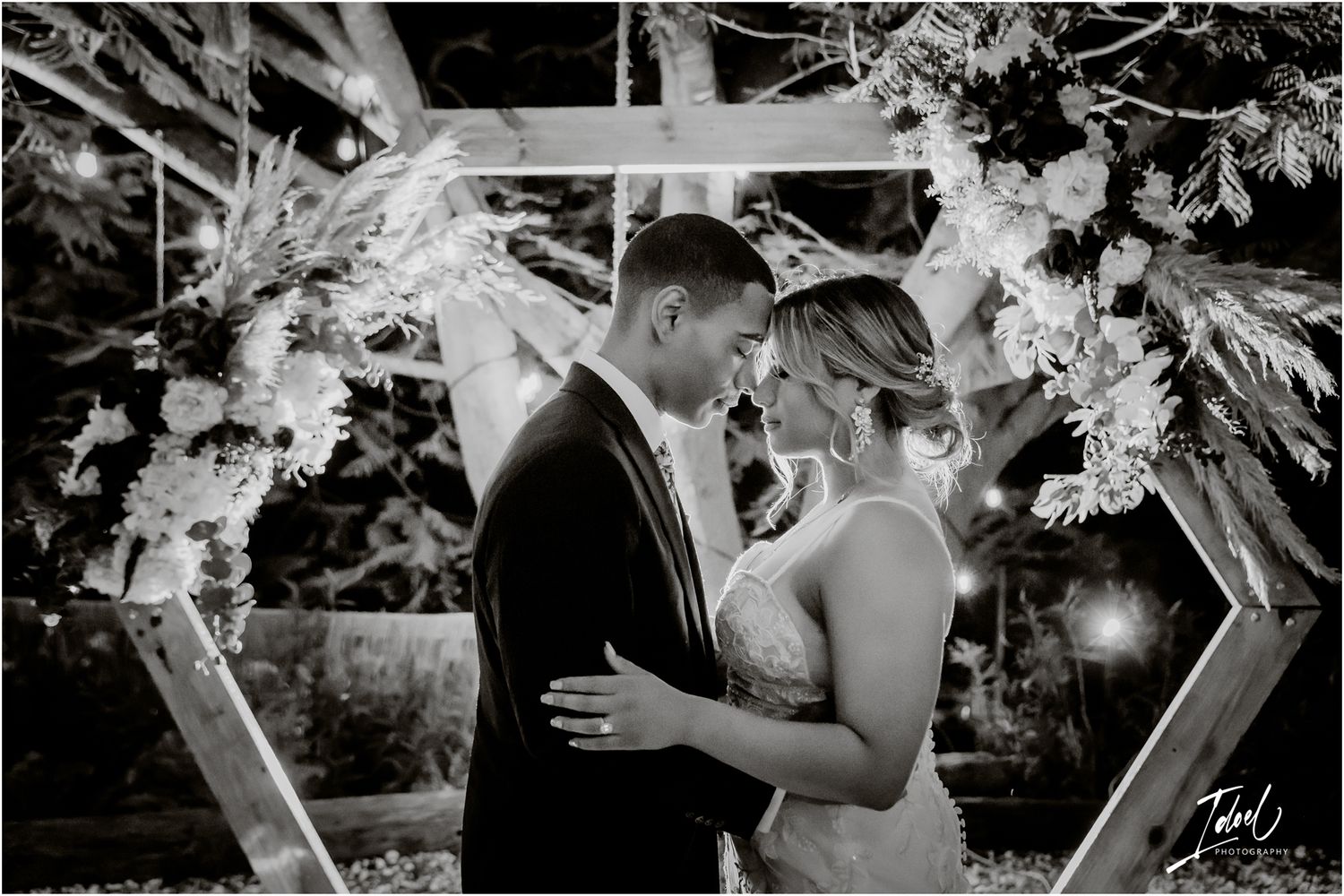 Romantic moment under a floral hexagon arch during an evening wedding ceremony.