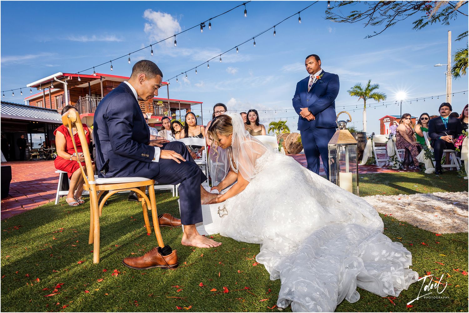Wedding guests watch as couple plays a fun game during outdoor reception with string lights overhead.
