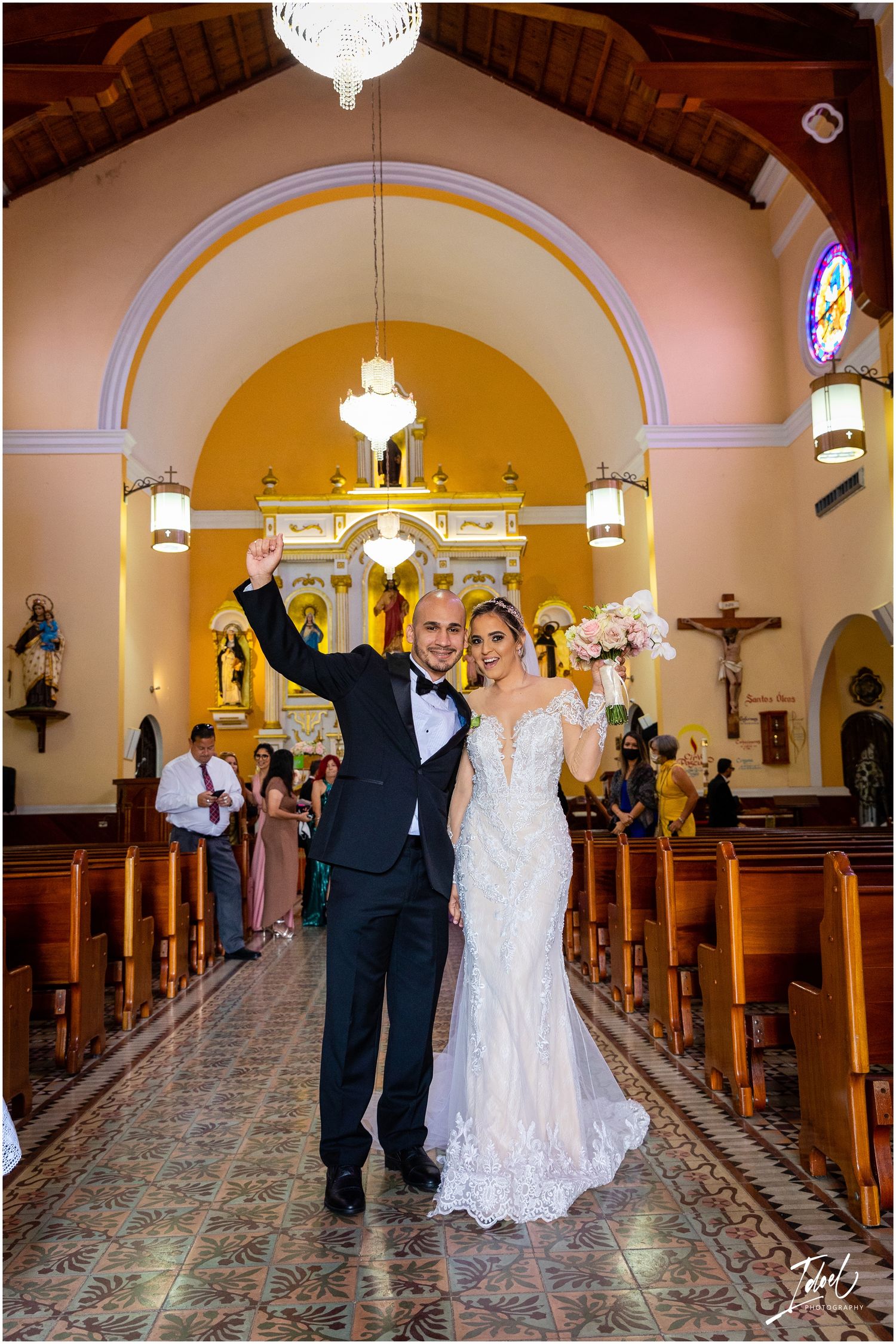 A wedding ceremony in a Catholic church with ornate arches and chandeliers as a couple celebrates at the altar.