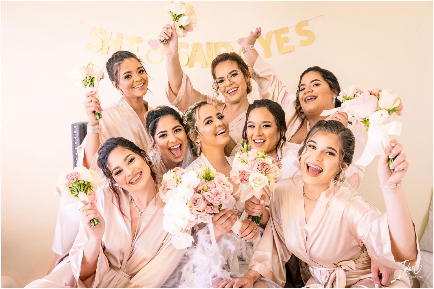 Bridesmaids in pink robes celebrating with champagne under gold party decorations.