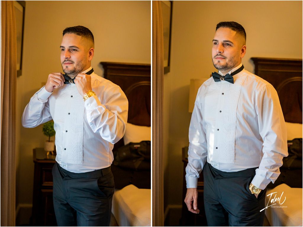 A person wearing a white dress shirt and black bow tie adjusts their collar while getting dressed in formal attire.