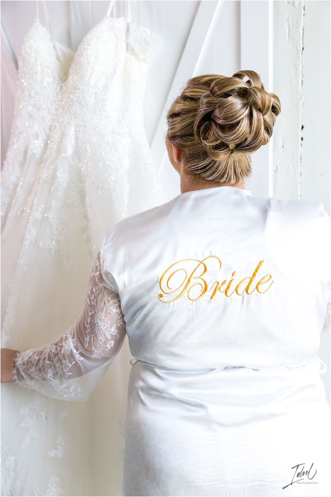 White satin robe with gold 'Bride' lettering shown from behind with wedding dress in background.