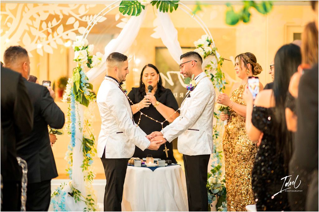 Wedding ceremony takes place under beautiful decorative lighting and greenery as guests watch the intimate celebration.