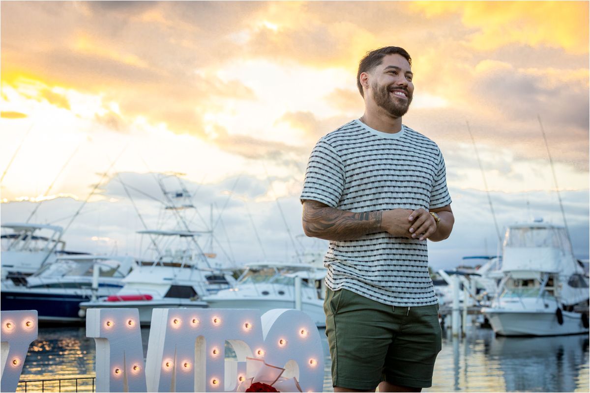 Someone stands on a dock at sunset with boats and yachts moored in the marina behind them.
