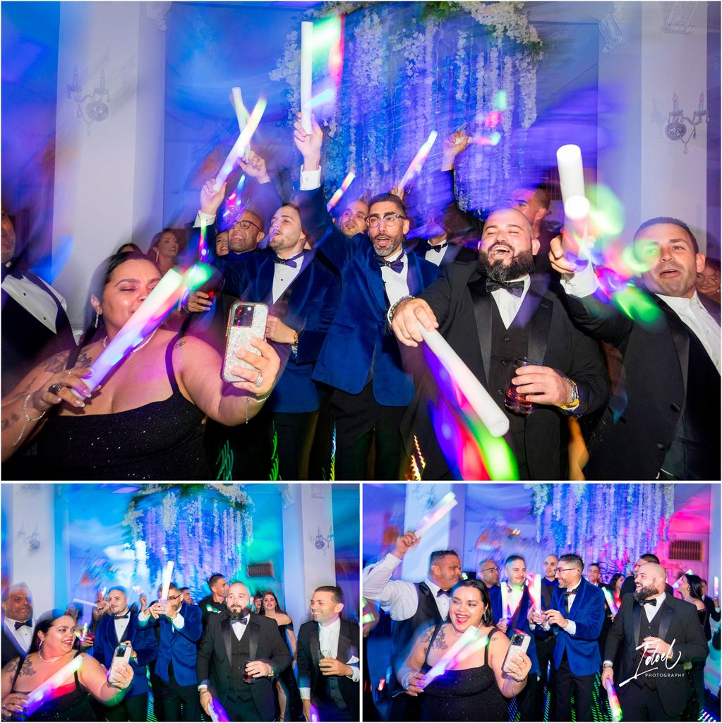 Wedding guests wave colorful glow sticks during reception party with blue and purple uplighting in elegant venue.