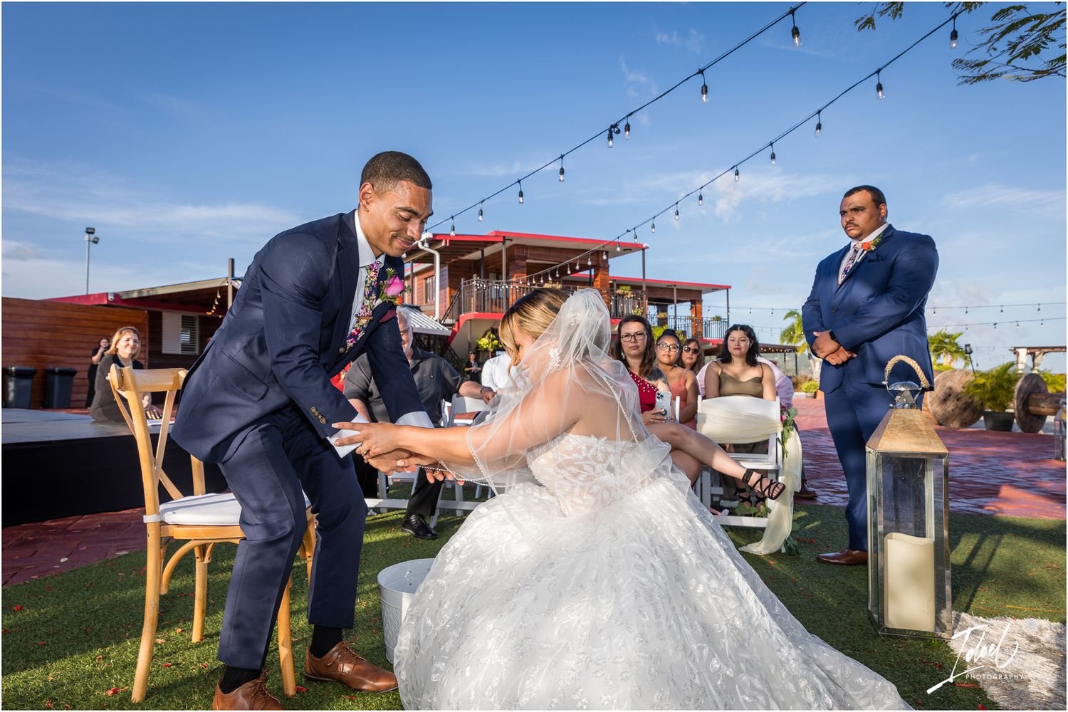 Joyful moment during wedding reception game on outdoor patio under string lights.