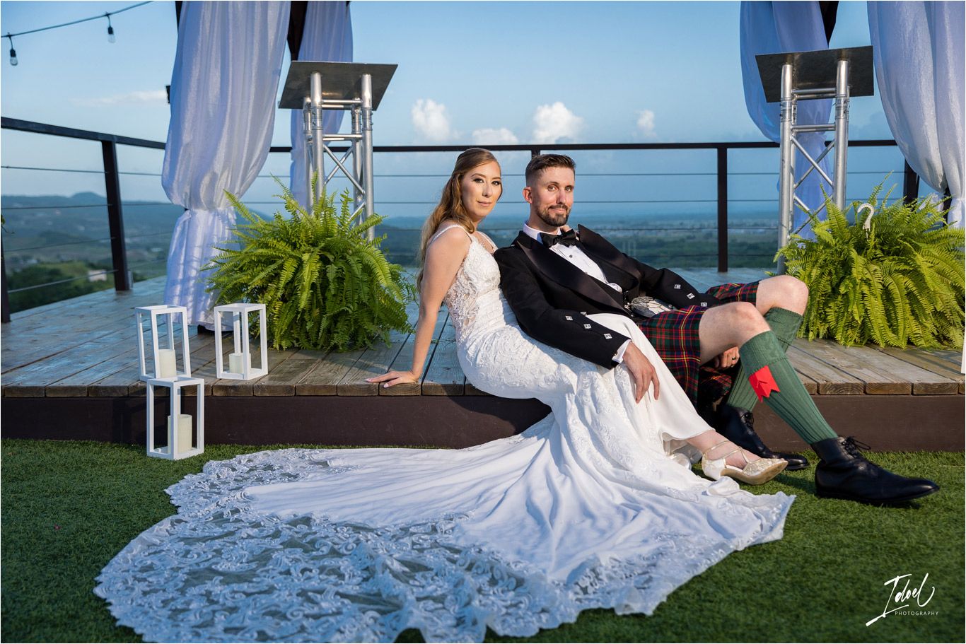 Couple relaxes on artificial turf under decorated pergola with mountain views and string lights.