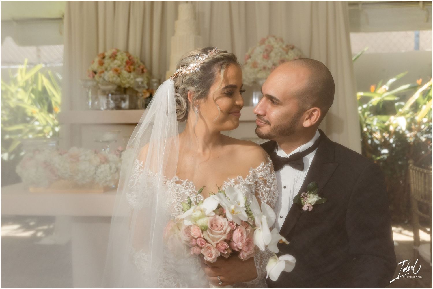 Intimate wedding portrait with soft lighting and pink floral bouquet against cream backdrop.
