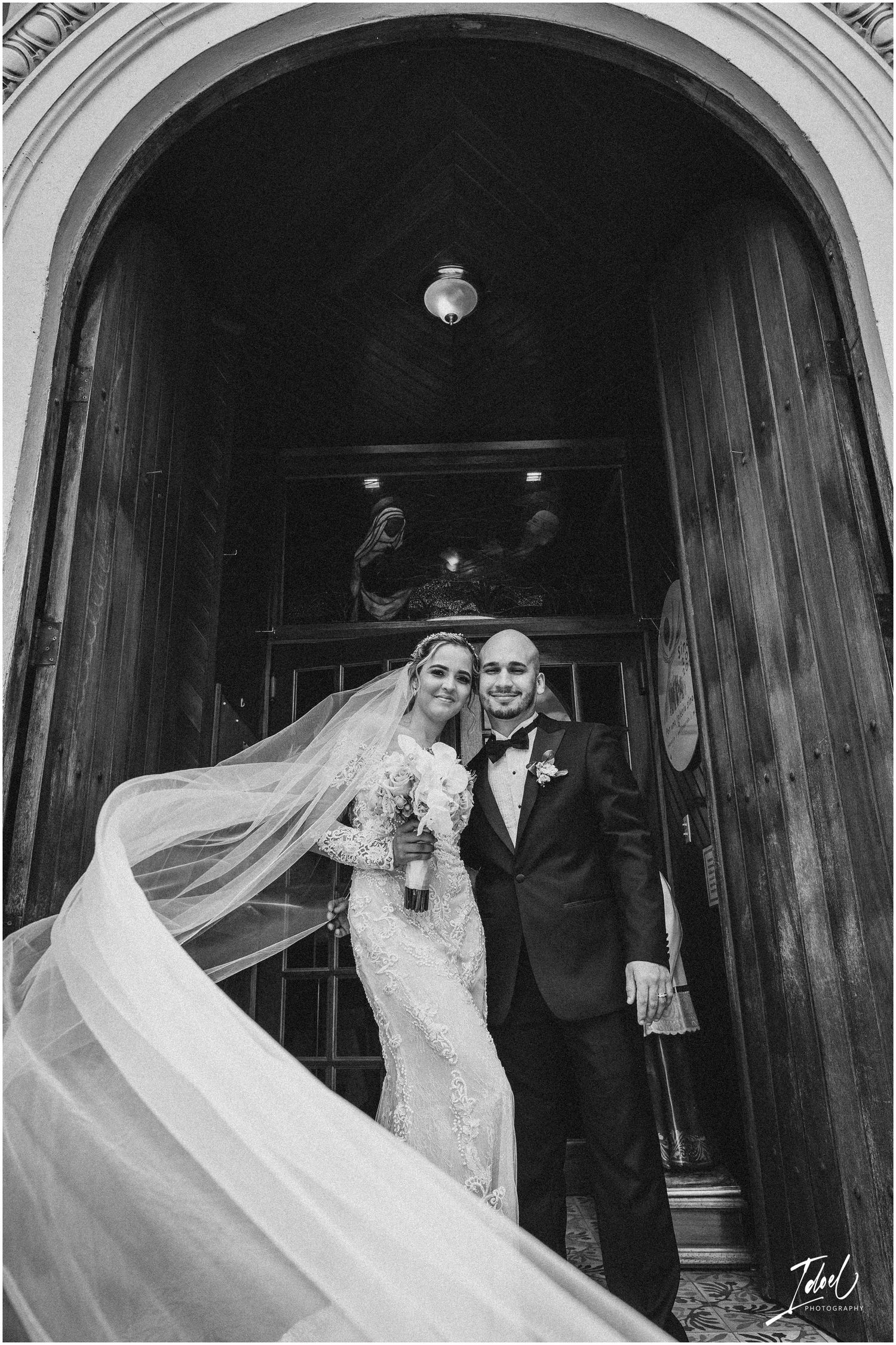A dramatic black and white photo showing a bride's flowing veil under a cathedral archway.
