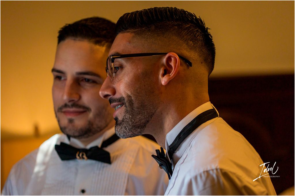 Two gentlemen in formal white shirts and bow ties share an intimate moment in warm lighting.