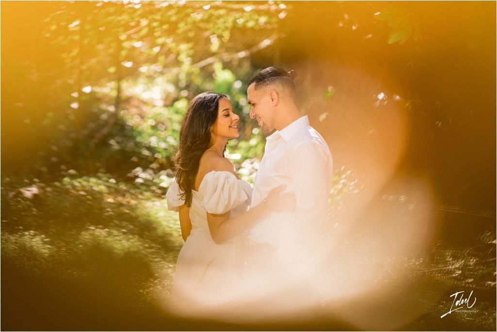 Romantic wedding photo captured through soft golden bokeh effect in a garden setting during sunset.