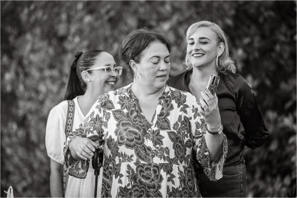 Three people share a candid joyful moment together outdoors, laughing and smiling in black and white photography.