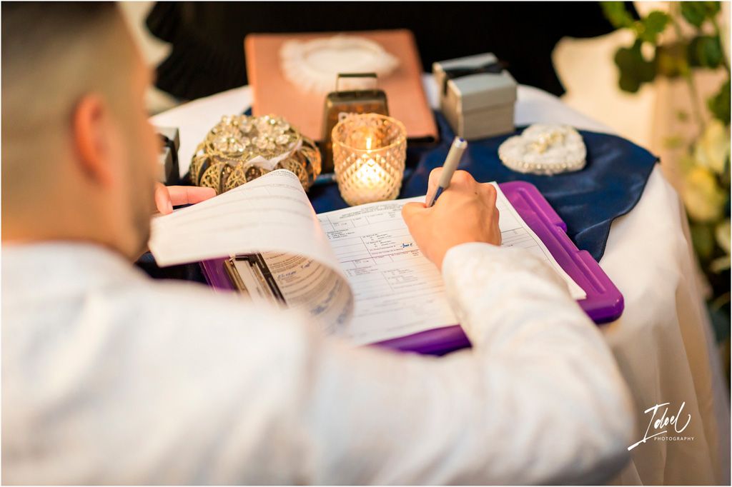 A person writing on white paper with a votive candle and purple accents on a decorated wedding table.