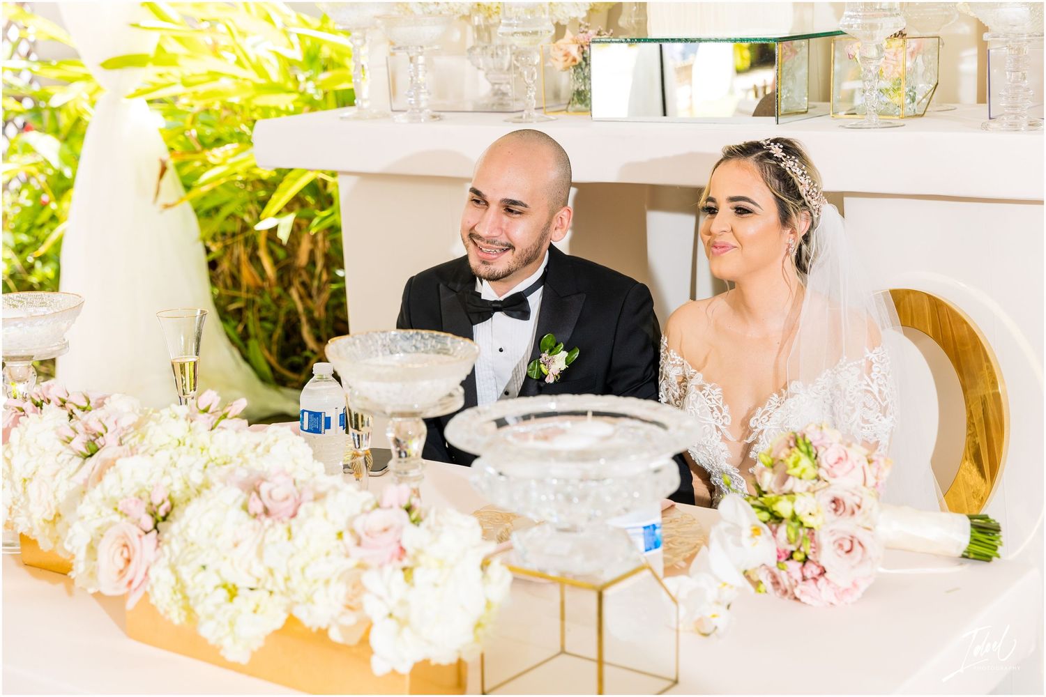 A newlywed couple shares a moment at their elegantly decorated reception table with white floral centerpieces.
