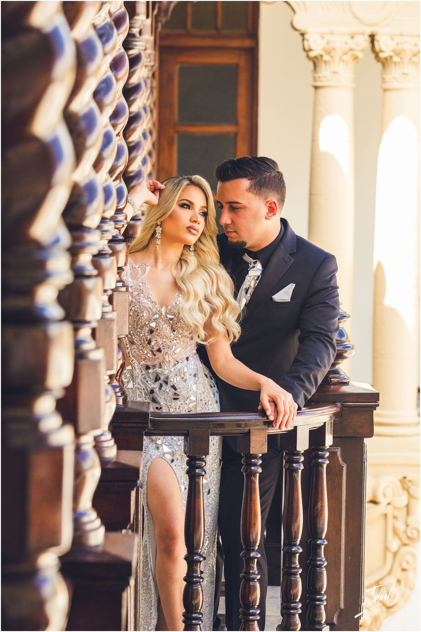 Elegant couple poses by ornate wooden railing in formal evening wear.