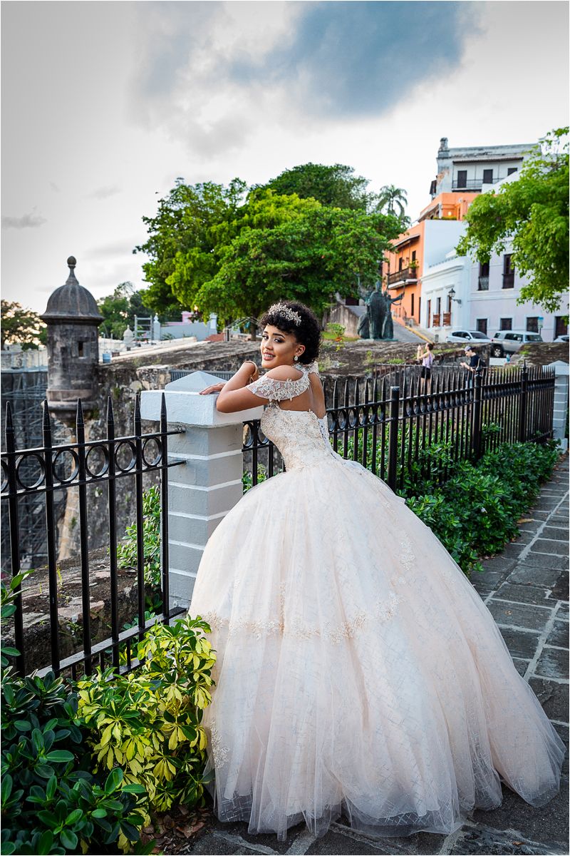 A stunning wedding dress with a voluminous tulle skirt photographed against a historic stone wall and lush greenery.
